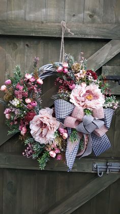 a wreath hanging on the side of a wooden door decorated with pink flowers and greenery