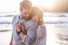 a man and woman embracing each other on the beach at sunset with the ocean in the background