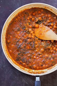 a pot filled with beans and spinach on top of a black counter next to a wooden spoon