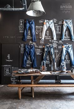 several pairs of jeans are hanging on a blackboard in front of a wooden bench