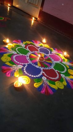 candles are lit on the floor in front of a colorful rangolite with flowers