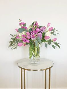 a vase filled with pink and white flowers sitting on top of a table next to a wall