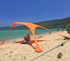 a man sitting under an orange tent on the beach