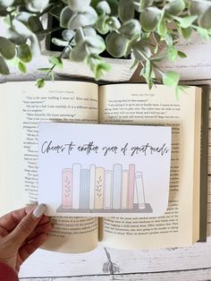 someone is holding up an open book with books on it and flowers in the background