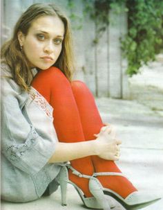 a woman sitting on the ground with her legs crossed and wearing high heels, looking at the camera