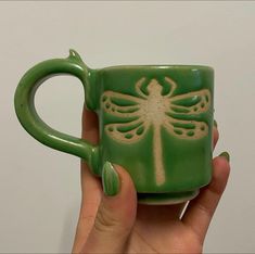 a hand holding a green mug with a dragon on it