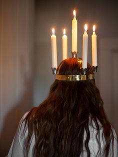 a woman with long hair wearing a crown made of lit candles on her head, in front of a mirror