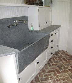 a kitchen with white cabinets and grey counter tops, an apron style sink in the center