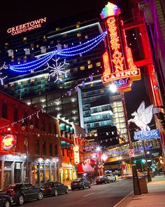 a city street filled with lots of traffic next to tall buildings covered in christmas lights