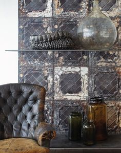 a leather chair sitting in front of a wall with decorative tiles on it and vases