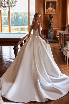 a woman in a white wedding dress standing on a wooden floor next to a chandelier