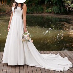 a woman in a white dress and hat standing on a wooden dock next to water