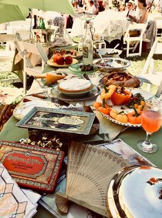 an outdoor table with many plates and food on it, including pies, oranges, and other foods