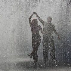 two people standing in front of a fountain with water spouting all around them