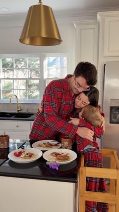 a man and woman in pajamas hugging each other at the kitchen counter with food on plates