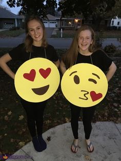 two girls in black shirts are holding yellow emotictive smiley faces with hearts on them