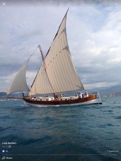 a sailboat with two people on it floating in the blue ocean under cloudy skies