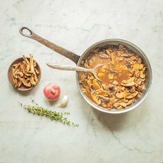 a pot filled with mushrooms next to an apple and spoon on a counter top,