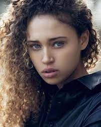 a close up of a person with curly hair wearing a black shirt and looking at the camera