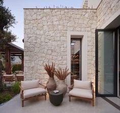 two chairs and a vase sitting on the outside of a house next to a stone wall