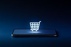 a cell phone with a shopping cart on it sitting in front of a screen that is lit up