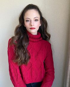 a woman in a red sweater is posing for the camera with her hands on her hips