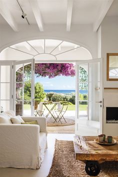 an open living room with white furniture and purple flowers on the ceiling over looking the ocean