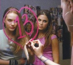 two young women standing in front of a mirror with pink writing on the side of them