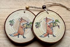 two wood slices with pictures of foxes on them, hanging from twine strings against a wooden surface