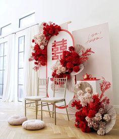 red and white flowers are arranged on the wall next to two chairs in front of a sign