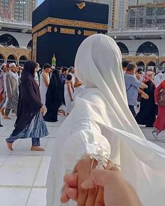 a woman in a white veil is holding her hand up to the camera while people walk by