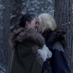 two women standing next to each other near a tree in the snow with fur on their shoulders