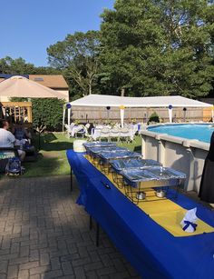 people sitting at tables in front of a pool with blue and yellow tablecloths