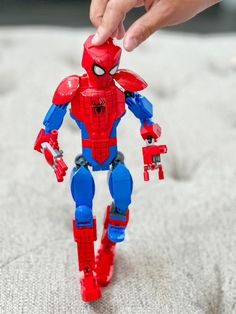 a hand is holding a toy that looks like a spider man on top of a bed