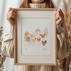 a woman holding up a framed painting with flowers and birds