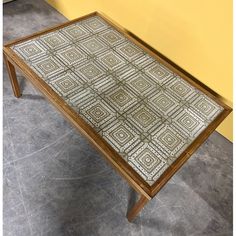 a wooden table with an intricate design on it's top and bottom, sitting in front of a yellow wall