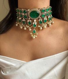 Inspired by the opulent designs of Sabyasachi, this emerald green Victorian choker set is the epitome of elegance and timeless beauty. The choker, meticulously crafted, features a central emerald stone surrounded by intricate gold filigree work that echoes the grandeur of the Victorian era. Each detail is a testament to the exquisite craftsmanship, with tiny pearls and delicate gold beads enhancing the necklace's regal appeal. Complementing the choker are a pair of matching earrings that mirror the necklace's luxurious design. The earrings feature a smaller version of the choker's central emerald, encircled by the same intricate gold detailing and pearls, offering a cohesive and sophisticated look. The emerald's deep green hue provides a striking contrast against the shimmering gold, creat Indian Choker Necklace Set, Victorian Choker, Unique Wedding Jewelry, Indian Choker, Indian Choker Necklace, Neck Pieces Jewelry, Sabyasachi Jewellery, Pearl Jewelry Design, Indian Jewelry Sets