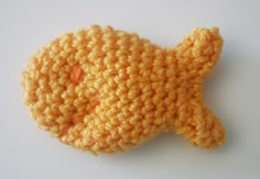 an orange crocheted fish brooch sits on a white surface, ready to be sewn