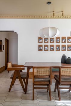 a dining room table with four chairs and pictures on the wall above it, along with two vases