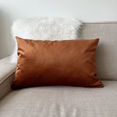 a brown pillow sitting on top of a couch next to a white fur covered pillow