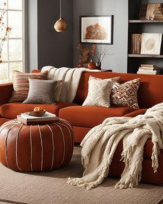 a living room with orange couches and pillows on the floor in front of a window