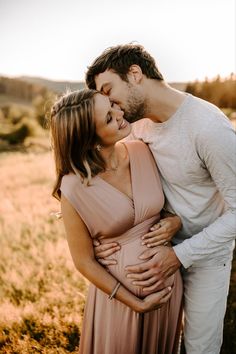 a pregnant couple cuddles in an open field