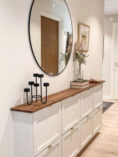 a room with white cabinets and a round mirror on the wall above it is a vase with flowers