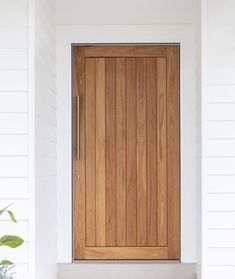 a wooden door on the side of a white house with potted plants next to it