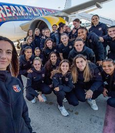 a group of women standing in front of an airplane with their arms around each other