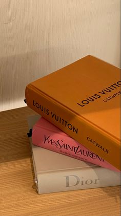 three books stacked on top of each other in front of a white wall and wooden floor