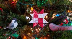 two christmas ornaments hanging from a tree with lights in the background and one bird on it