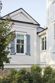 a white house with blue shutters on the windows and bushes in front of it