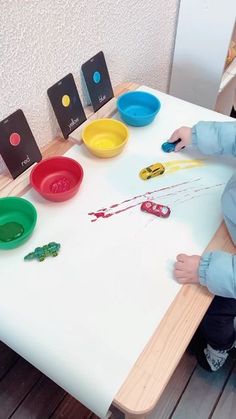 a little boy sitting at a table playing with some plastic cups and spoons on it