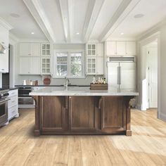 a large kitchen with white cabinets and wood flooring, along with an island in the middle